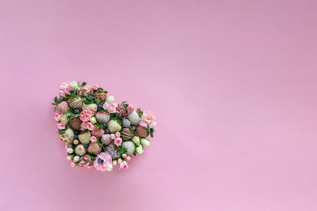 Hartvormige doos met handgemaakte chocolade bedekte aardbeien met verschillende toppings en bloemen als een geschenk op Valentijnsdag op roze achtergrond met vrije ruimte voor tekst