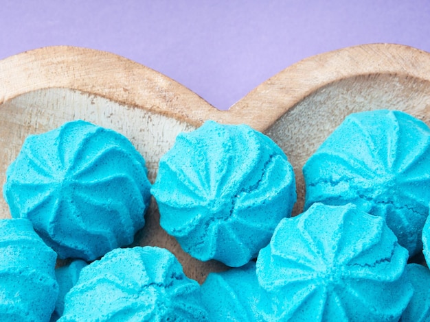 Hartvormige houten schaal met blauwe zoete meringues op paars