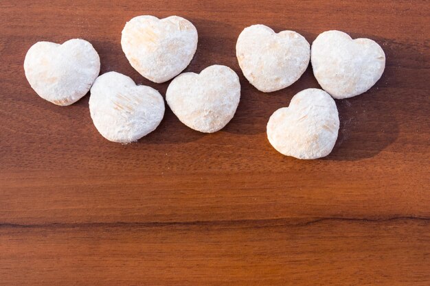 Hartvormige koekjes bedekt met poedersuiker op houten tafel. Bovenaanzicht, kopieer ruimte