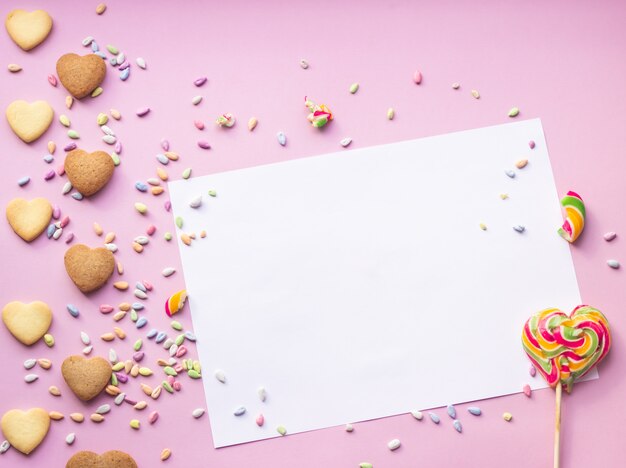 Hartvormige koekjes en kleurrijke hagelslag met blanco papier en lolly