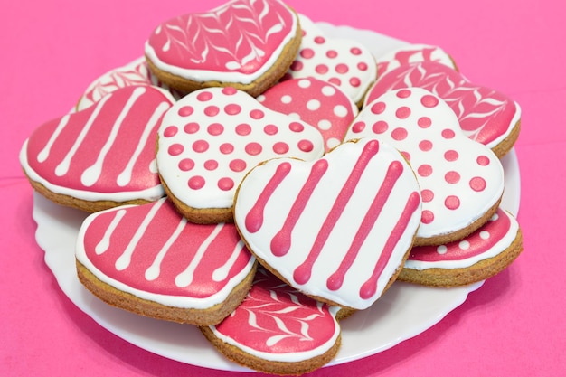 hartvormige koekjes met stippen en strepen op een bord op de roze achtergrond, close-up