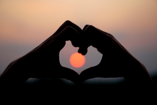 Hartvormige menselijke hand silhouet zonsondergang achtergrond