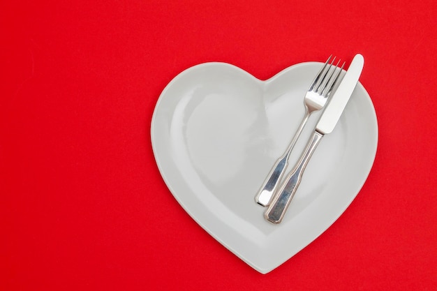 Hartvormige plaat met mes en vork op een rode achtergrond