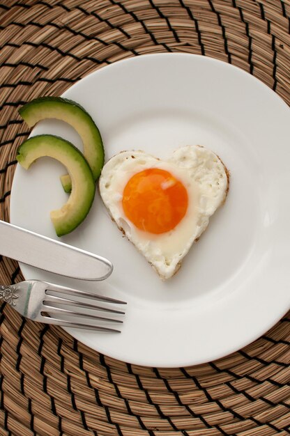 Hartvormige roereieren op een wit bord met plakjes avocado en bestek