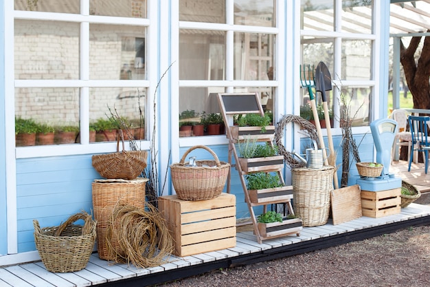 Harvest concept. Wicker baskets next to garden equipment by the wall of a blue country house. The decor of the courtyard of a country house. Gardening concept. Autumn harvest of plenty.