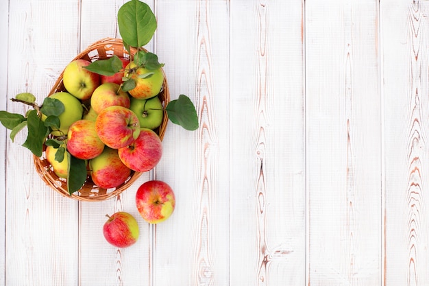 Harvest of fresh apples in straw basket on white wooden table