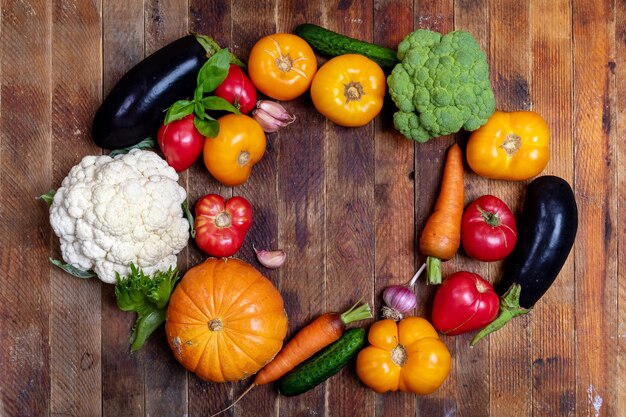 Photo harvest of fresh farm vegetables is laid out in oval on rustic wooden table top view copy space