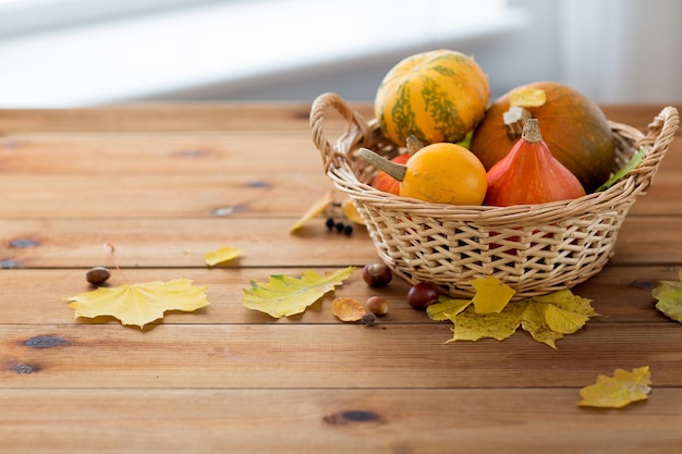 収穫、季節、広告、秋のコンセプト – 枝編み細工品バスケットにカボチャをクローズアップし、自宅の木のテーブルの上に葉を置く