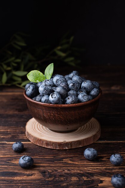 Harvest of summer berries, ripe blueberries with water drops in a bowl on a dark wooden background, healthy food.