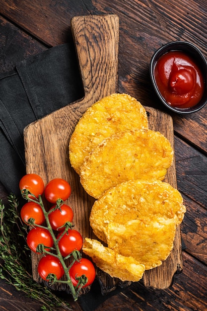 Hash brown potato potato patties on a wooden board with ketchup\
wooden background top view