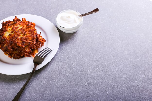 Hash brown and sour cream on a plate against a gray stone background