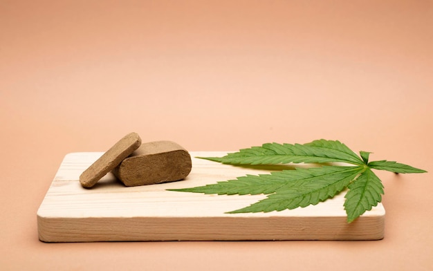 Compressa di hashish porzione di hashish da 100 grammi con una grande foglia di marijuana su fondo di legno marrone