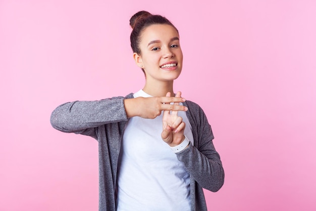 Hashtag internet populariteit portret van vrolijke trendy tienermeisje met knot kapsel in casual kleding met hash-symbool met vingers glimlachen naar camera studio opname geïsoleerd op roze achtergrond