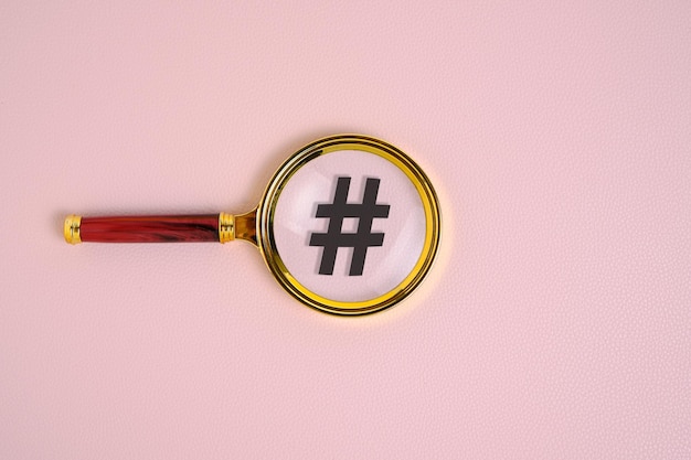 Hashtag symbol under magnifying glass on pink background