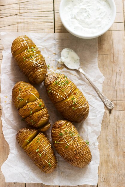 Hasselback potatoes served with cheese and sour cream sauce on a wooden table. Rustic style.