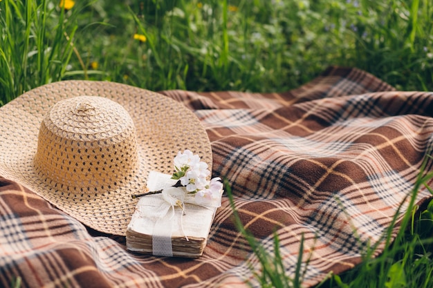 Шляпа и книга лежат на одеяле во время пикника в цветущем весеннем яблоневом саду