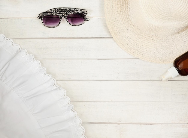 Hat and glasses part of a white dress on a white wooden
background flat lay top view