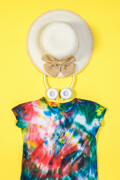 Hat headphones and tie dye tshirt on a yellow background Flat lay