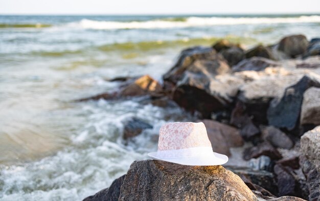 The hat lies on the stones near the sea shore under the summer setting sun