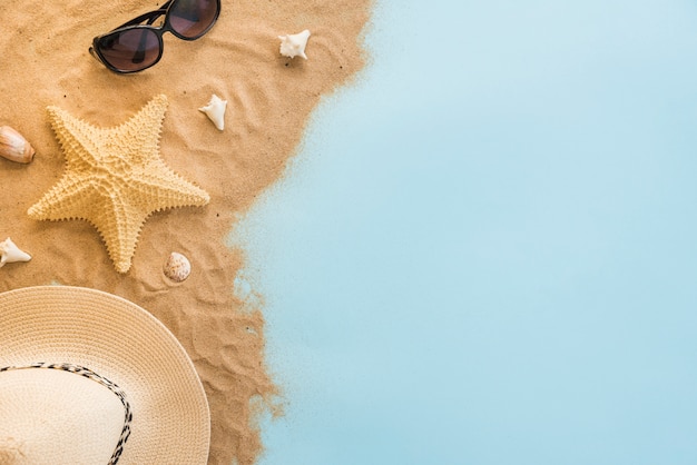 Hat near sunglasses and seashells on sand