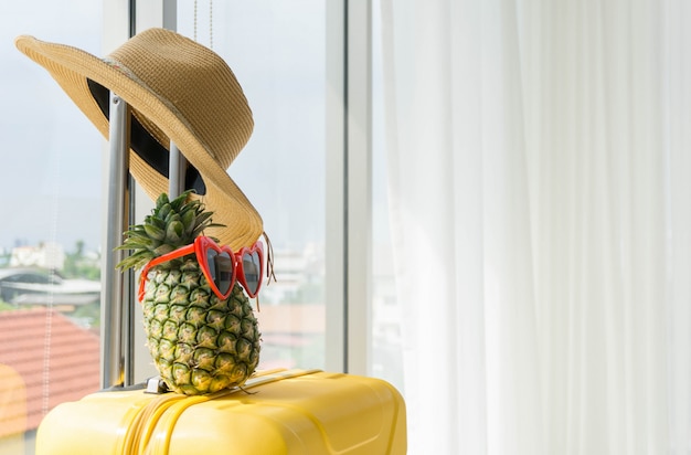 Hat and pineapple on suitcase in hotel with copy space