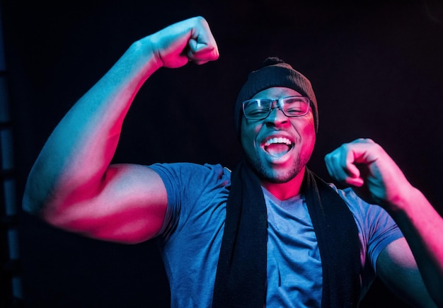 In hat and scarf Futuristic neon lighting Young african american man in the studio