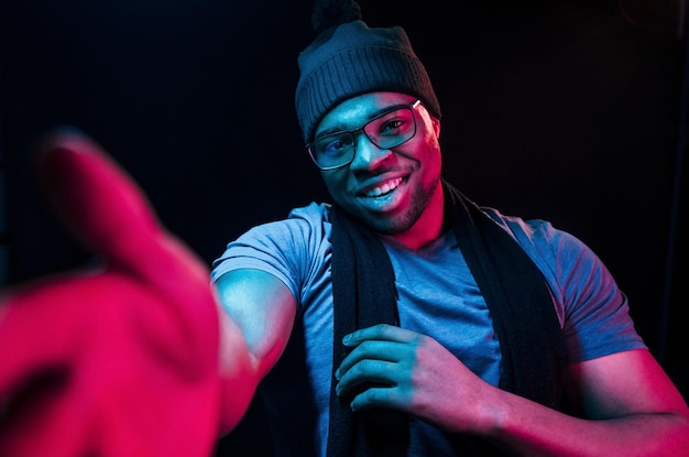 In hat and scarf Futuristic neon lighting Young african american man in the studio