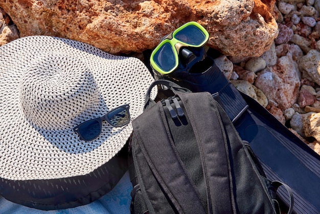 돌 해안에 마스크가 달린 모자, 선글라스, 배낭 및 지느러미.