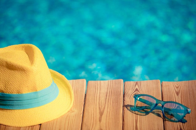 Hat and sunglasses on wood against blue water background Summer vacation concept