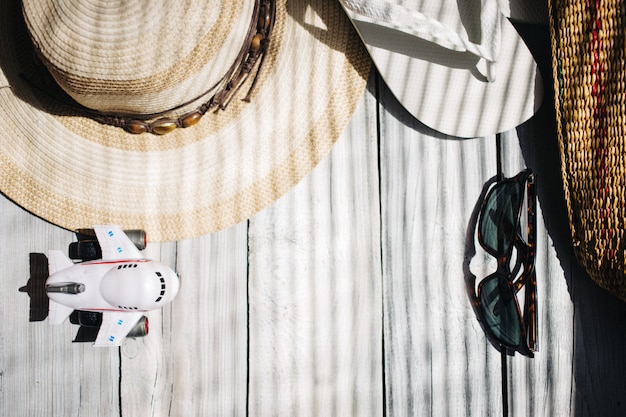 Un cappello, infradito bianco, occhiali da sole, aereo, una borsa da spiaggia sullo sfondo bianco in legno