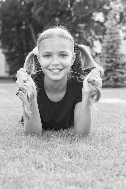 Have fun Girl cute kid laying green grass Healthy emotional happy kid relaxing outdoors What makes child happy Girl ponytails hairstyle enjoy relax Cheerful schoolgirl Happy smiling pupil