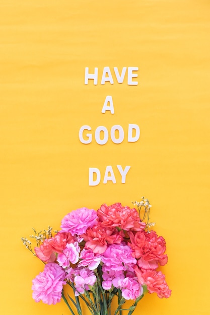 Have a good day  wooden word  with fresh flowers carnations on bright yellow background