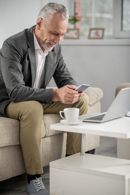 Have a look. Attentive man sitting on his sofa and bowing head while using his gadget