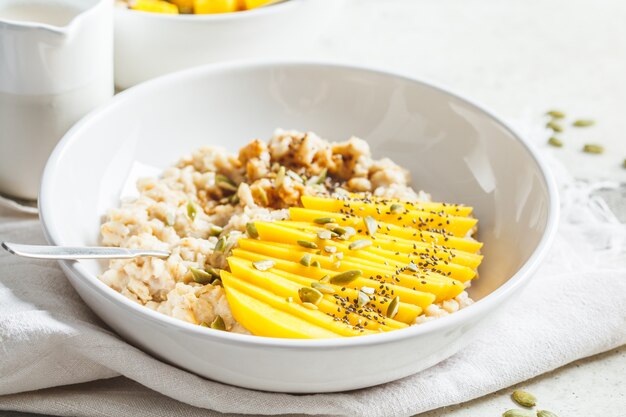 Havermout met mango en pompoenpitten in witte kom. Gezond ontbijt, veganistisch eten.