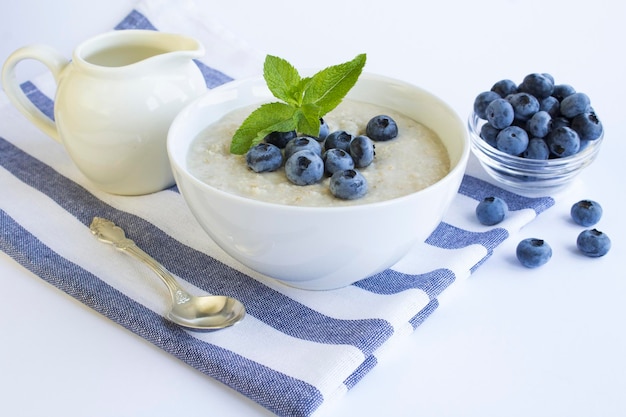 Havermout met melk en bosbes in de witte kom op de witte achtergrond Gezond ontbijt