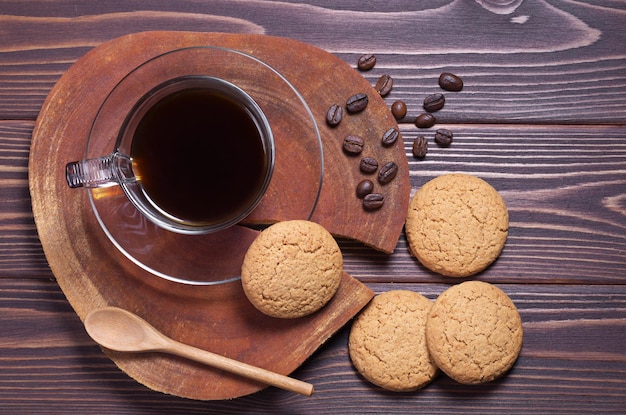 Havermoutkoekjes en zwarte koffie in een transparante kop op bruine houten ondergrond, bovenaanzicht