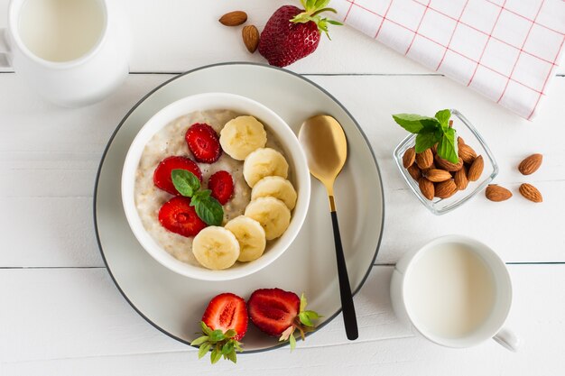 Havermoutkom met banaan en aardbei, melkglas op een witte tafel. gezonde biologische voeding.