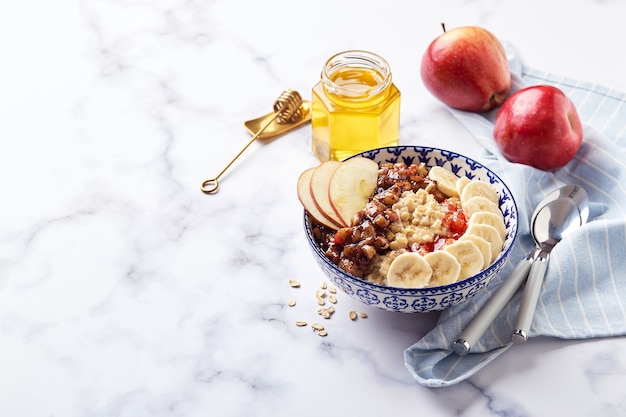 Havermoutpap met gekarameliseerde appels met kaneel, banaan, geraspte aardbeien en honing op lichte marmeren achtergrond