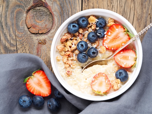 Havermoutpap met verse aardbeien, bosbessen, muesli op oude rustieke houten achtergrond.