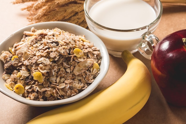 Havermoutvlokken in een kom, een melk, een appel en een banaan op houten lijst. Gezond ontbijtconcept.