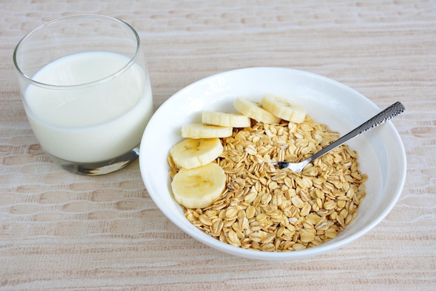 Havermoutvlokken met banaanplakken in witte kom en theelepeltje, close-up