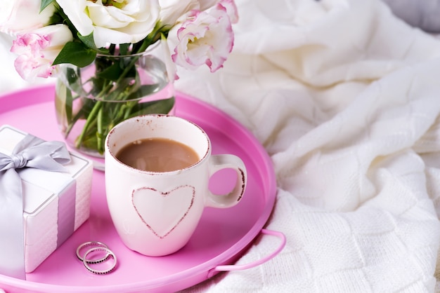 Having a cup of coffee with chocolate, flowers eustoma and gift box on tray on blanket in bed.