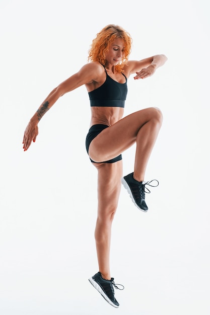 Having exercise. Redhead female bodybuilder is in the studio on white space.