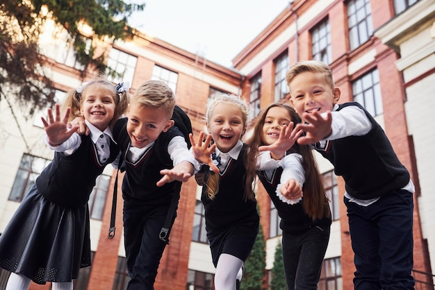 Foto divertirsi e abbracciarsi. gruppo di ragazzi in uniforme scolastica che è insieme all'aperto vicino all'edificio scolastico.