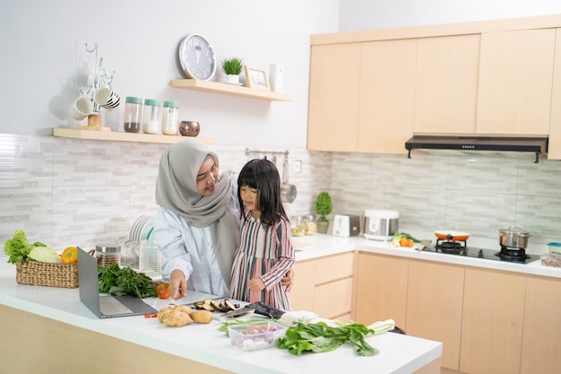 Having fun muslim woman with hijab and kid preparing dinner together