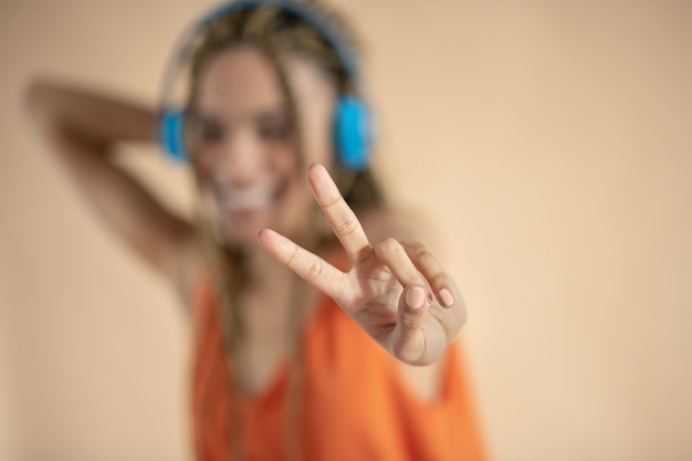 Having fun. Smiling young African American female in blue headphones, listening to music, showing peace sign