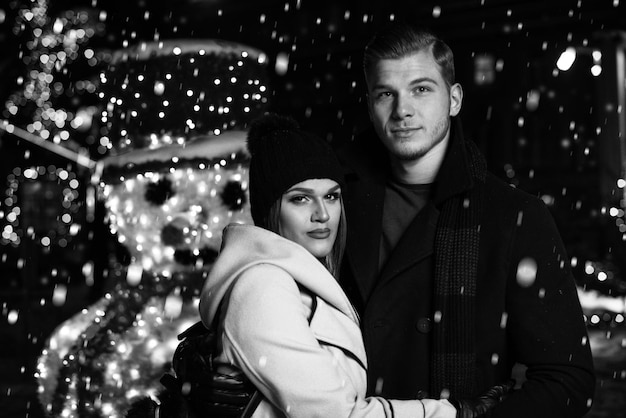 クリスマスの妖精で一緒に楽しんでいる若い陽気なカップルは、お互いを見て笑う暖かい服を着て楽しんで散歩をしています