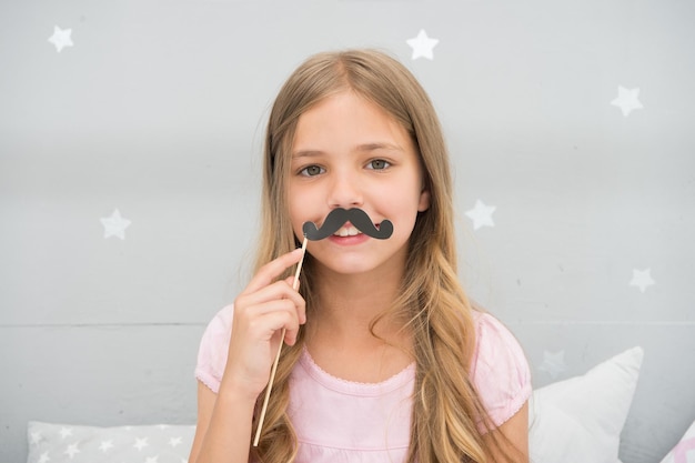 Having fun with fake mustache Happiness and humor concept Kid long hair happy smile face Girl carefree child having fun with mustache Play with mustache photo booth props Hair care and beauty
