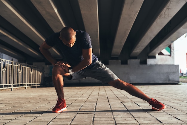 Having a good stretch. Handsome young African man in sports clothing stretching while warming up outdoors