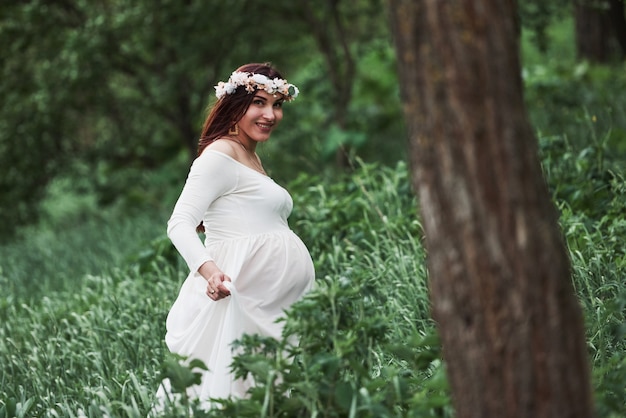 Having good time. Beautiful pregnant woman in dress have a walk outdoors. Positive brunette